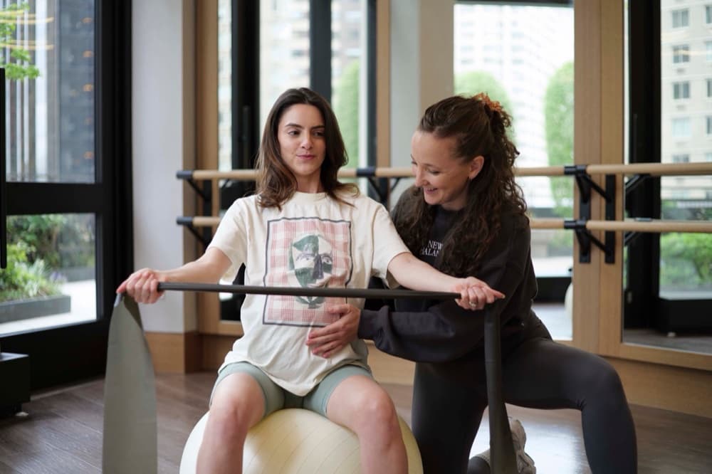 A Woma prenatal session — Lane guiding a client through resistance band work on a stability ball